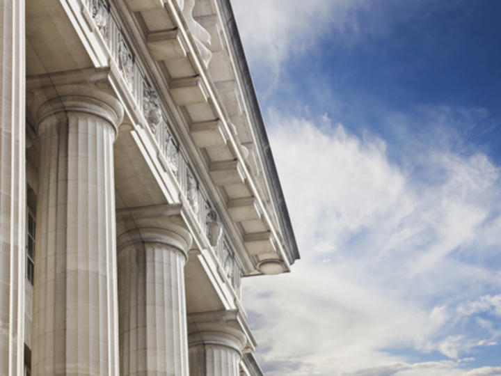 The side of a Courthouse building with large pillars and a blue sky and white clouds