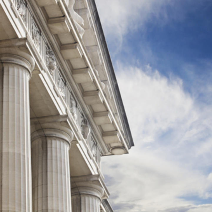 The side of a Courthouse building with large pillars and a blue sky and white clouds